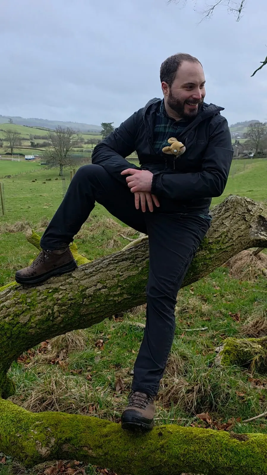 Marco Rapaccini sitting on a mossy fallen tree trunk in a green countryside landscape